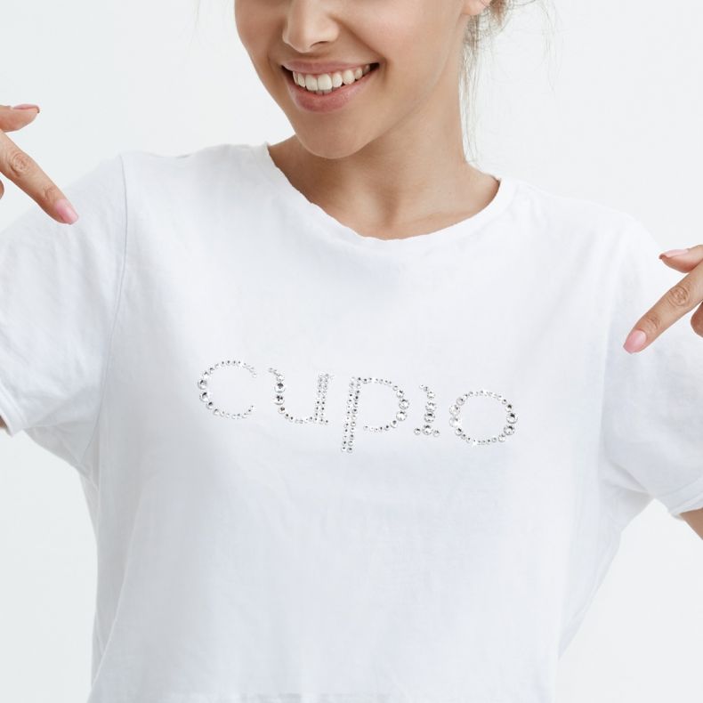 Junge Frau in einem weißen T-Shirt mit dem Schriftzug "CUPIO" aus Strasssteinen