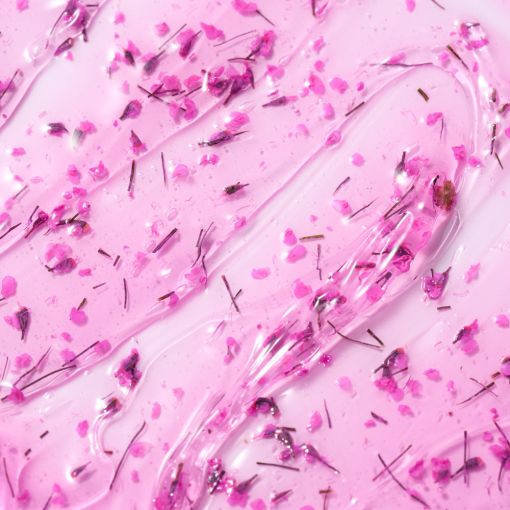Nahaufnahme einer rosa Gel- oder Creme-Textur mit Glitzerpartikeln und pinken Blütenstückchen, passend für ein Kosmetikprodukt