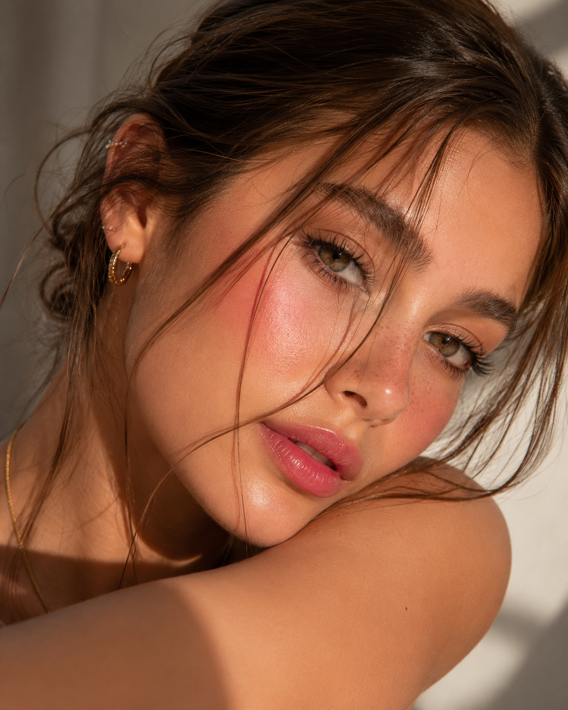 Porträt einer Frau mit goldenen Creolen und feiner Halskette, natürlichem Make-up und strahlendem Glow im warmen Sonnenlicht