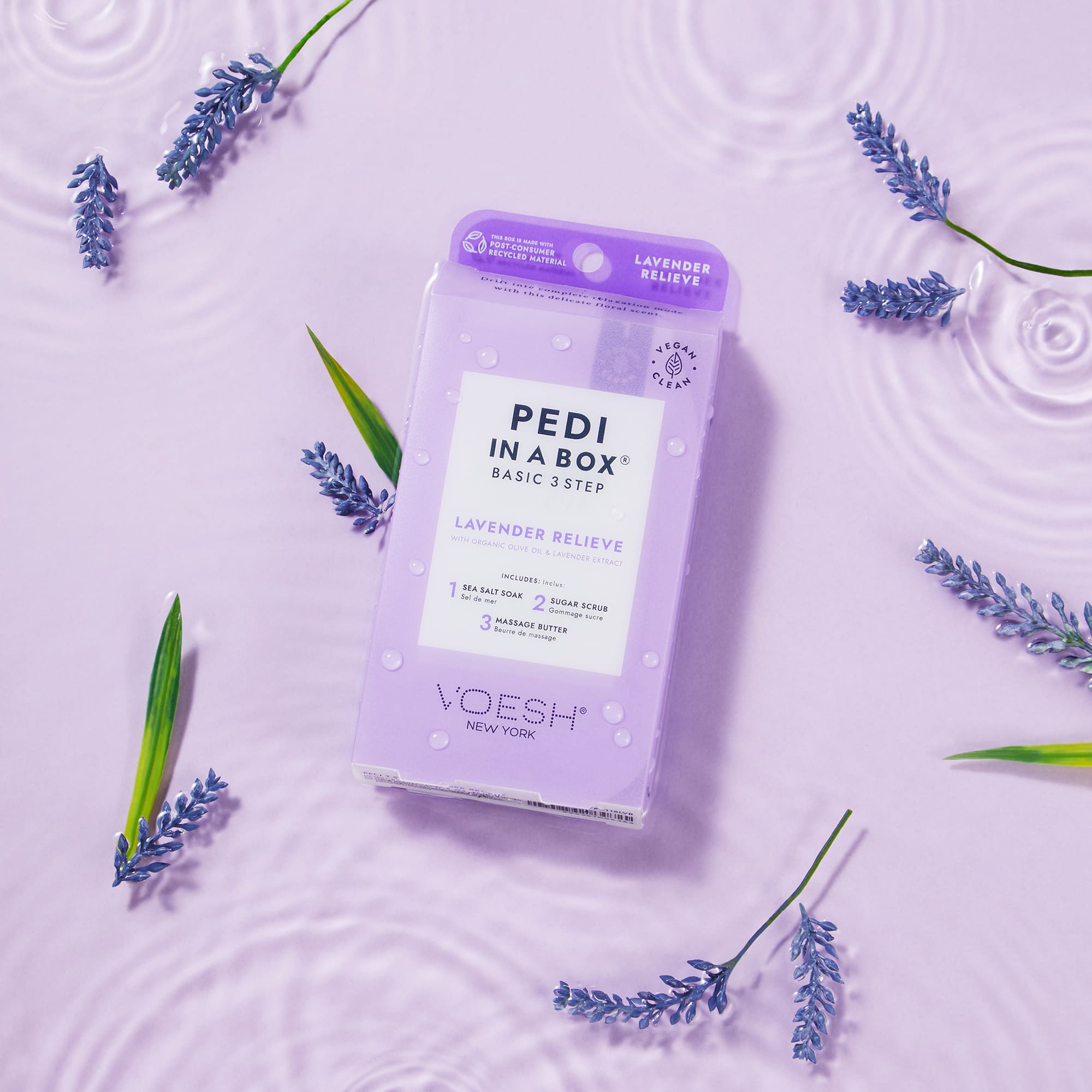 Voesh Pedi in a Box Basic 3 Step Lavender Relieve Packung auf lilafarbenem Untergrund mit Lavendelzweigen – 3-Step-Pediküre mit Meersalzbad, Zuckerpeeling und Massagebutter, beruhigend und pflegend