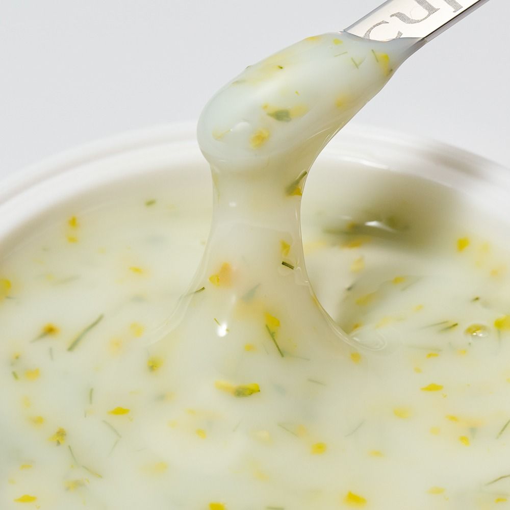 Nahaufnahme einer cremigen Kräutersoße mit feinen Kräutern und Gewürzstückchen auf einem Löffel