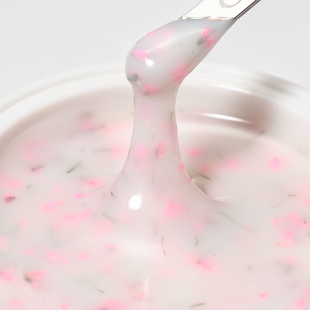 Nahaufnahme einer cremigen weißen Kosmetik-Gelmasse mit rosa Blütenpartikeln auf einem Spatel, ideal für Pflege- oder Beautyprodukte