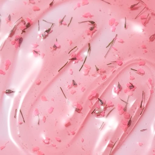 Nahaufnahme einer rosafarbenen Gel-Serum-Textur mit feinen Blüten- und Kräuterpartikeln, ideal zur Darstellung von Hautpflegeprodukten