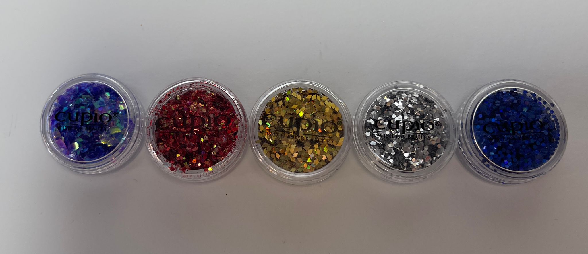 Fünf Dosen mit buntem Glitzer in verschiedenen Farben von Cupio auf weißem Hintergrund