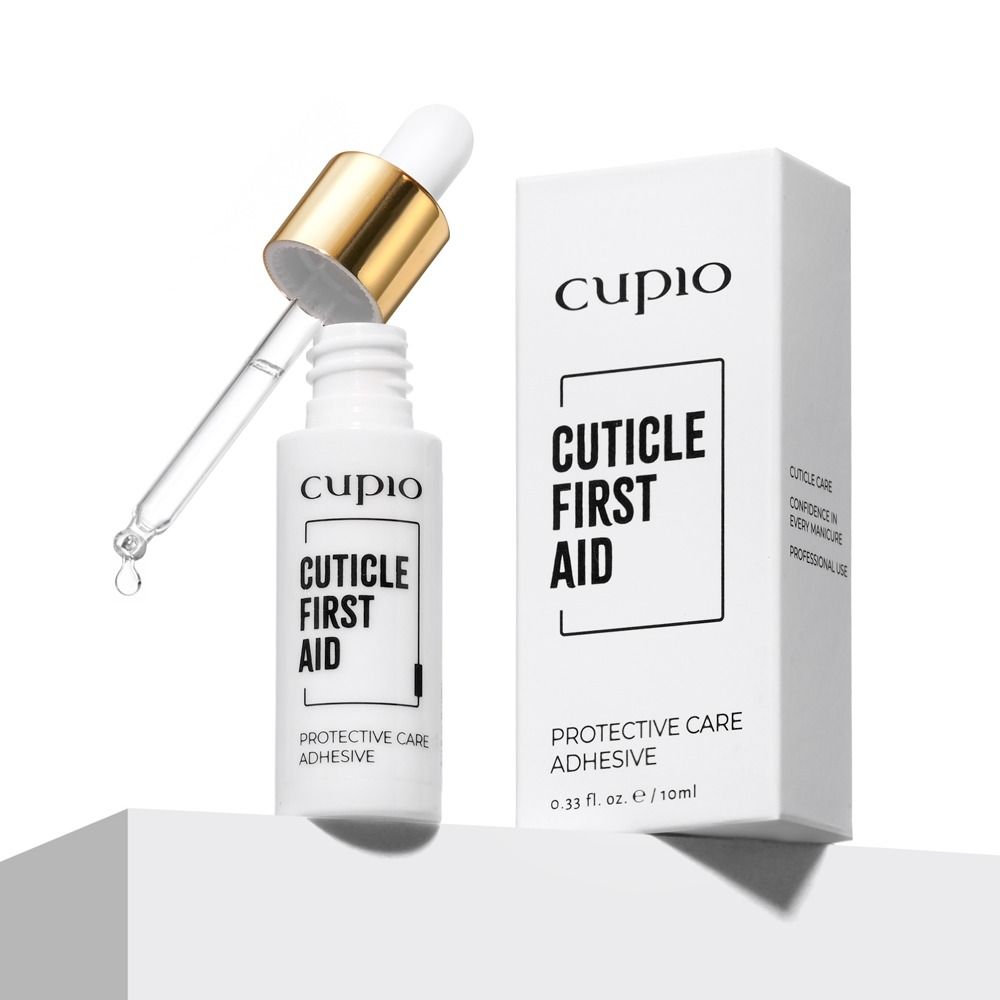 Geöffnete Flasche Cupio Cuticle First Aid Protective Care Adhesive mit Pipette und Tropfen neben der Produktverpackung für Nagelhautpflege