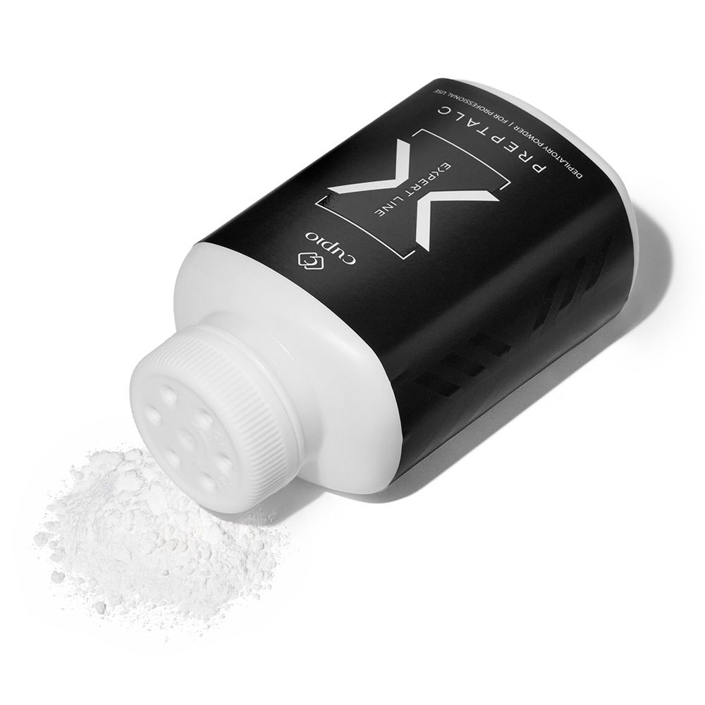 Schwarze Cuccio Pro X Expert Line Prep-Talc Flasche mit weißem Streuverschluss und etwas ausgestreutem weißen Puder auf hellem Hintergrund