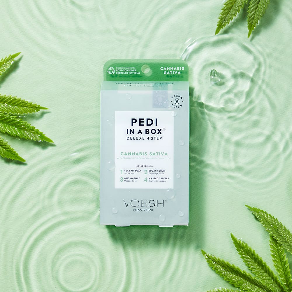 VOESH Pedi in a Box Deluxe 4 Step Cannabis Sativa mit Hanfsamenöl, Spa-Pediküre für empfindliche Haut, Produktpackung auf grünem Hintergrund mit Wasserwellen und Cannabisblättern