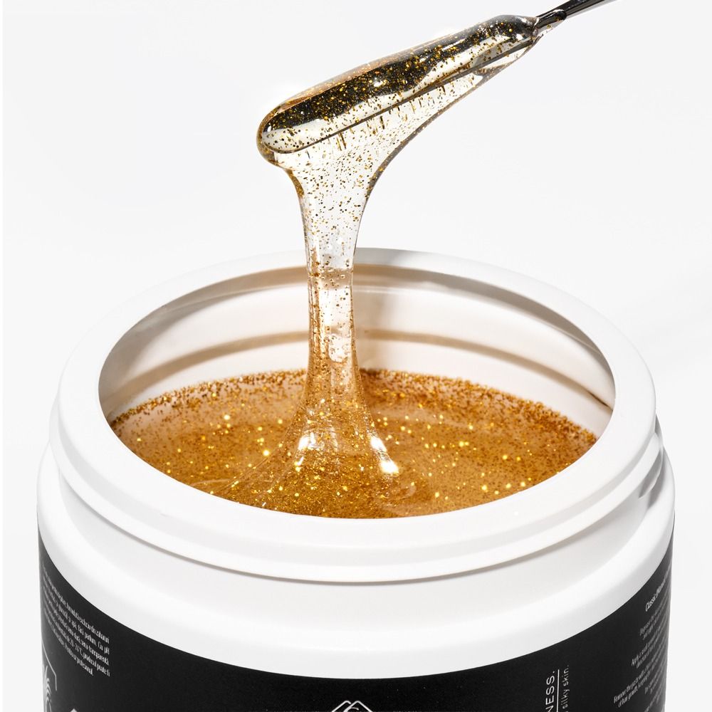 Nahaufnahme eines offenen Tiegels mit goldenem Glitzer-Waxinggel, das mit einem Spatel herausgezogen wird – Enthaarungsgel für professionelle Haarentfernung