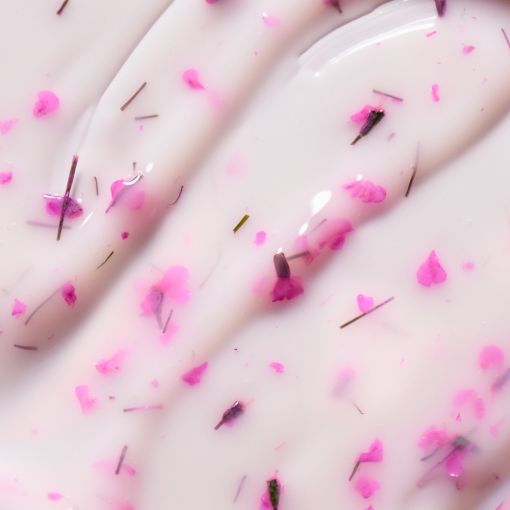 Nahaufnahme einer cremigen weißen Kosmetikmasse mit rosa Blütenstückchen und feinen Kräutern, ideal zur Darstellung eines natürlichen Pflegeprodukts