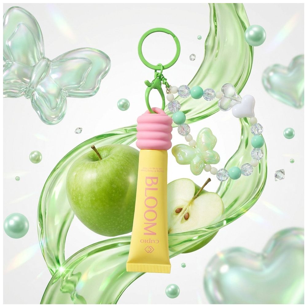 Cuccio Bloom Lipgloss als Schlüsselanhänger mit Perlenarmband, grünem Apfel und Apfelhälfte in schimmernder, verspielter Produktinszenierung