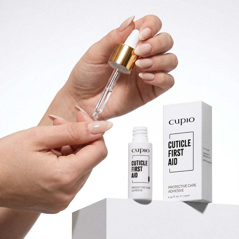 Hand trägt Cupio Cuticle First Aid mit Pipette auf die Nagelhaut auf; Nagelhautpflege und schützende Pflege mit Flasche und Verpackung