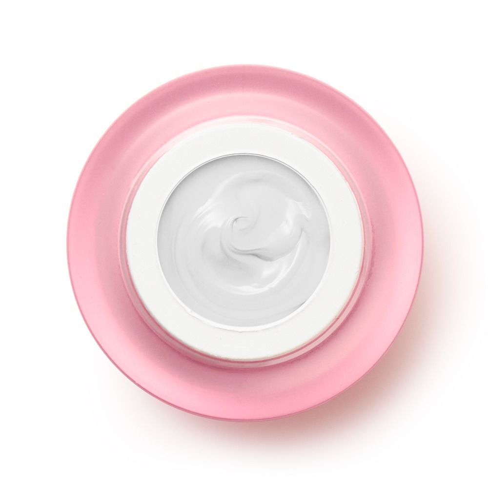 Draufsicht auf einen offenen Cremetiegel mit weißer Gesichtscreme und rosa Deckel auf weißem Hintergrund