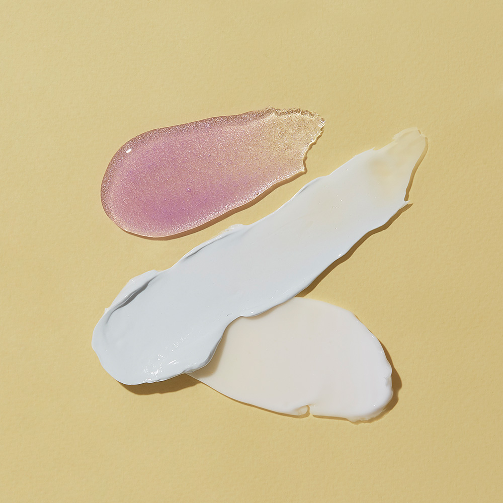 Nahaufnahme von schimmerndem rosa Serum und zwei weißen Creme-Texturen auf gelbem Hintergrund, ideal zur Darstellung von Hautpflegeprodukten