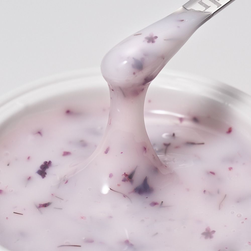 Nahaufnahme einer cremigen rosa Gesichtsmaske oder Körperpflege mit feinen Blütenpartikeln auf einem Spatel