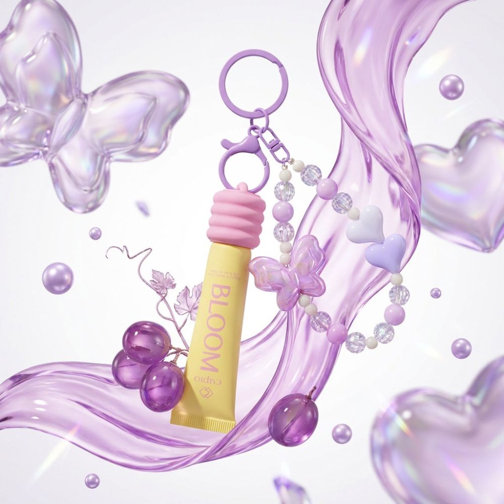 Gelber Bloom Lipgloss als Schlüsselanhänger mit rosa Kappe, lila Perlenkette und Schmetterling, inszeniert mit violetten Herzen und Trauben im Pastell-Look