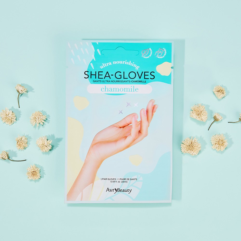 Verpackung der AvryBeauty Shea-Gloves Chamomile, ultra pflegende Handmaske mit Shea-Butter, auf hellblauem Hintergrund mit getrockneten Blüten