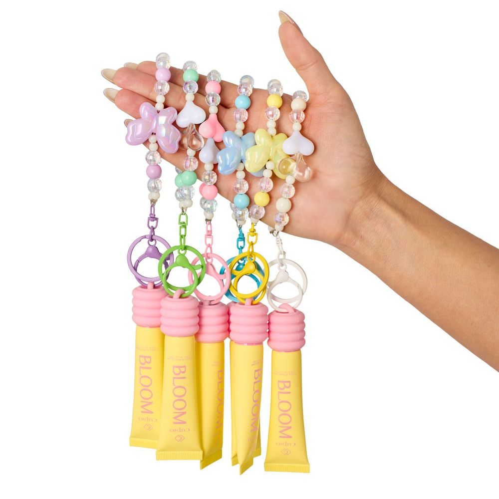 Hand hält mehrere Bloom Surprise Bag Überraschungs-Minis: Nagelhaut- und Handcremes in Reisegröße mit buntem Perlen-Charm zum Befestigen an Tasche oder Schlüsselbund.