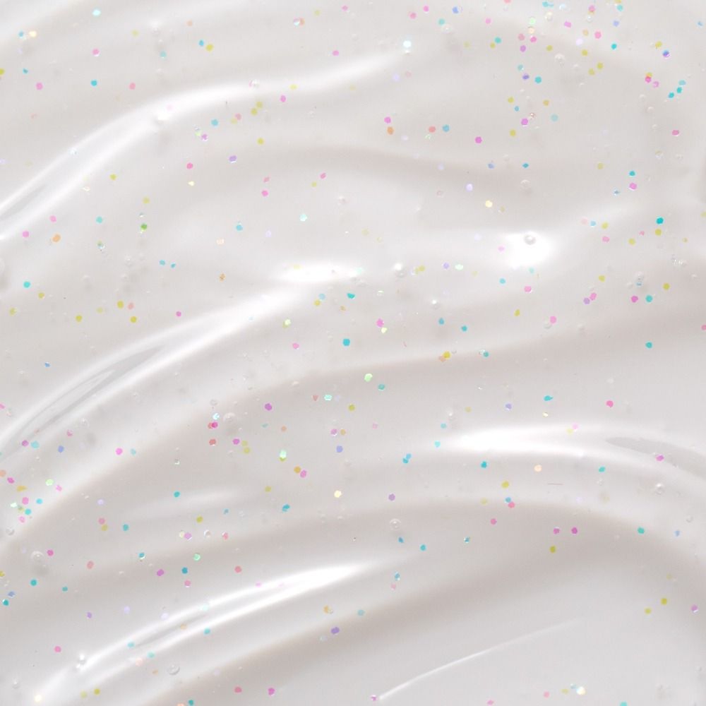 Nahaufnahme einer hellen Creme mit schimmernden, bunten Glitzerpartikeln auf einer glatten Oberfläche