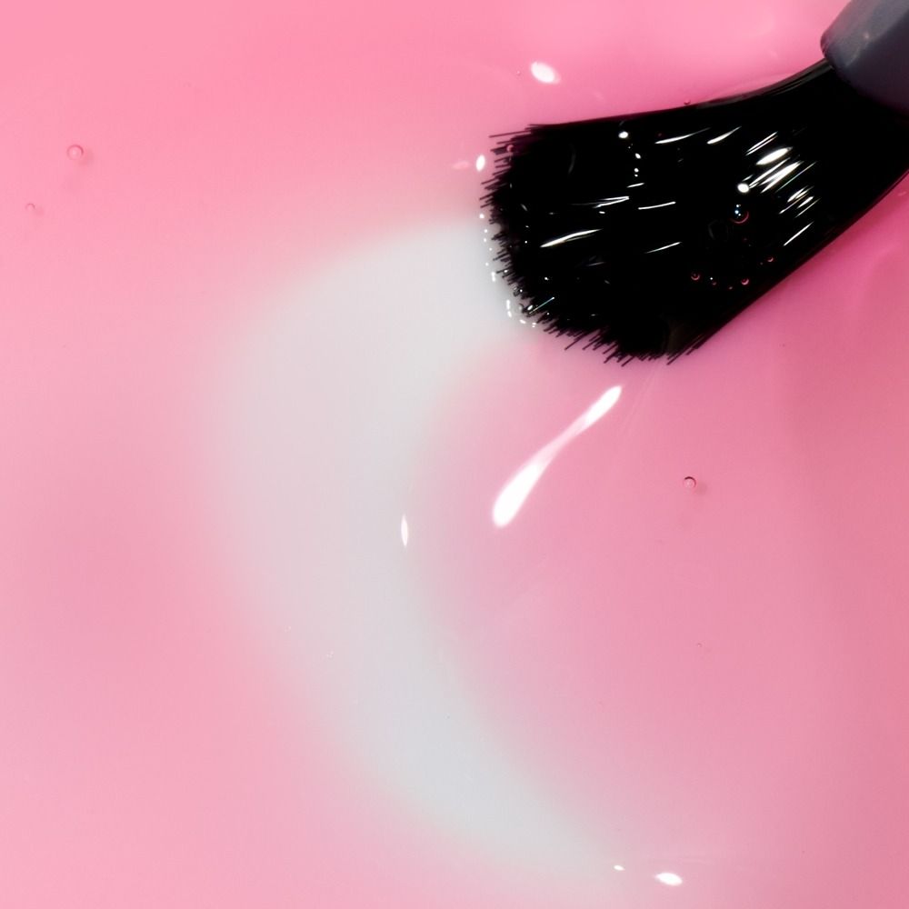 Schwarzer Pinsel trägt glänzenden rosa Nagellack auf – Detailaufnahme eines Kosmetikprodukts für Nägel und Maniküre