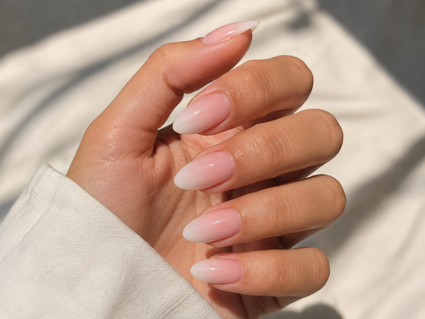 Nahaufnahme einer Hand mit mandelförmigen Kunstnägeln in zartem Rosa-Weiß Ombré und glänzender Oberfläche