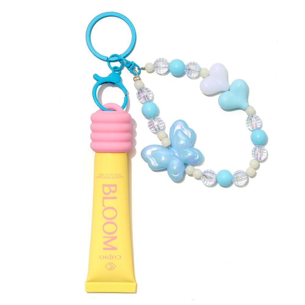 BLOOM Lipgloss als Schlüsselanhänger in Gelb mit rosa Kappe, blauem Ring und dekorativem Perlenband mit Schmetterling und Herzchen