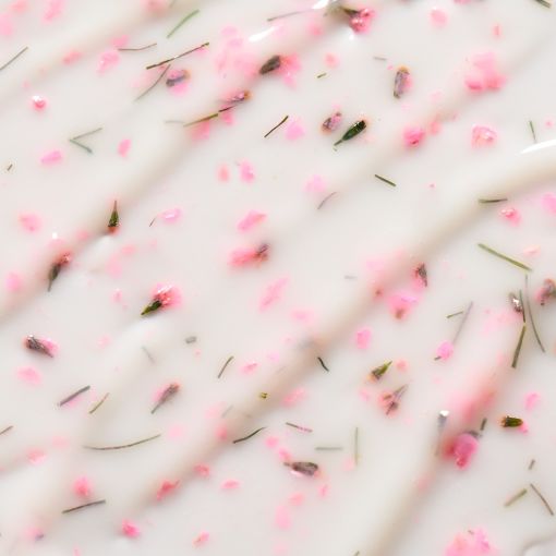 Detailansicht einer weißen Seife mit rosa Blütenstückchen und grünen Kräuterfasern