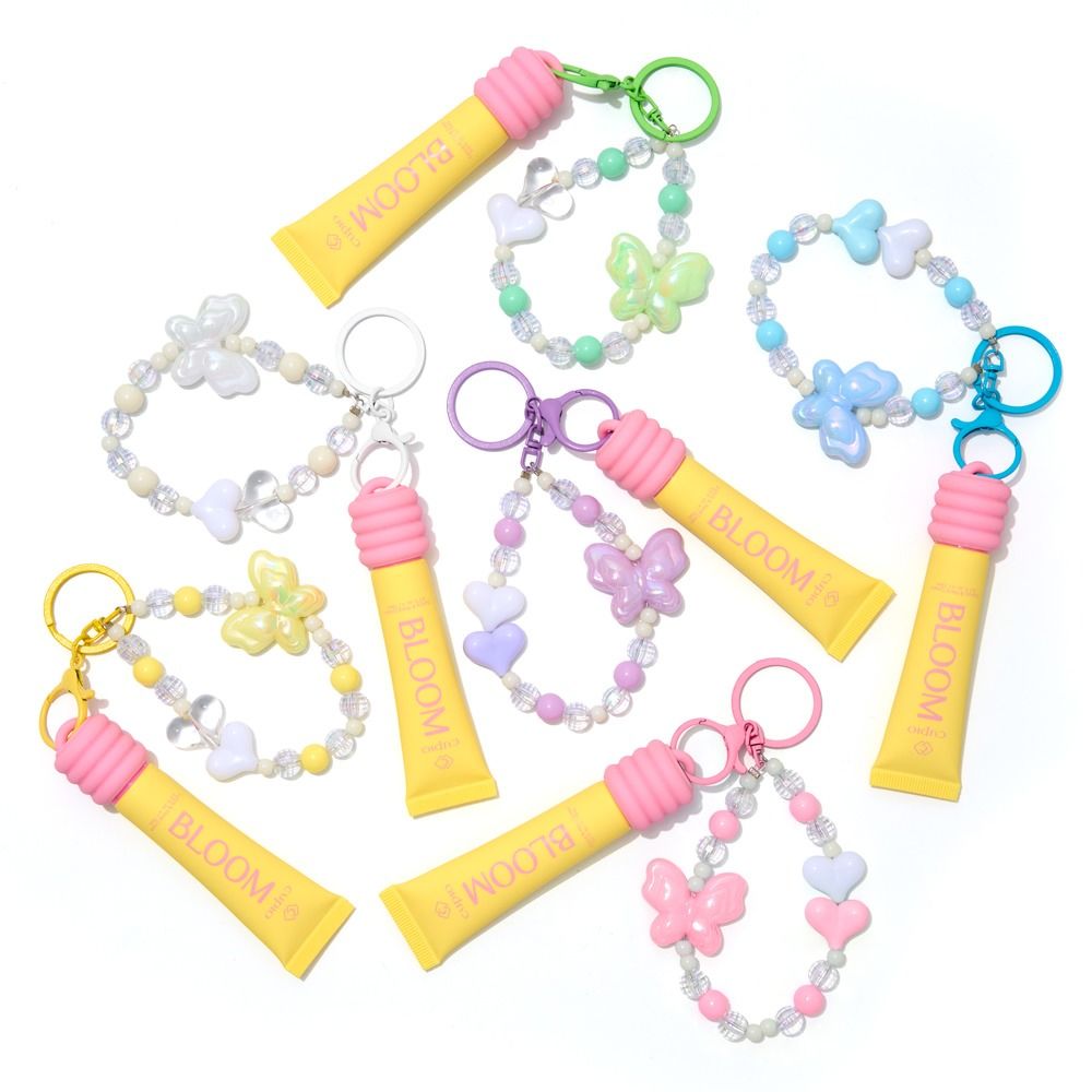 Mehrere BLOOM Lippenpflege-Schlüsselanhänger mit bunten Perlenarmbändern und Schmetterlingsanhängern in Pastellfarben auf weißem Hintergrund
