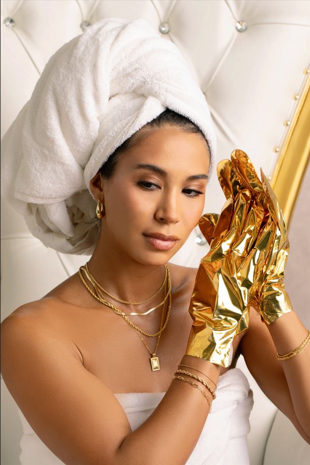 Frau im Spa-Look mit weißem Handtuch und goldenen Pflegehandschuhen als Beauty-Produkt für intensive Handpflege