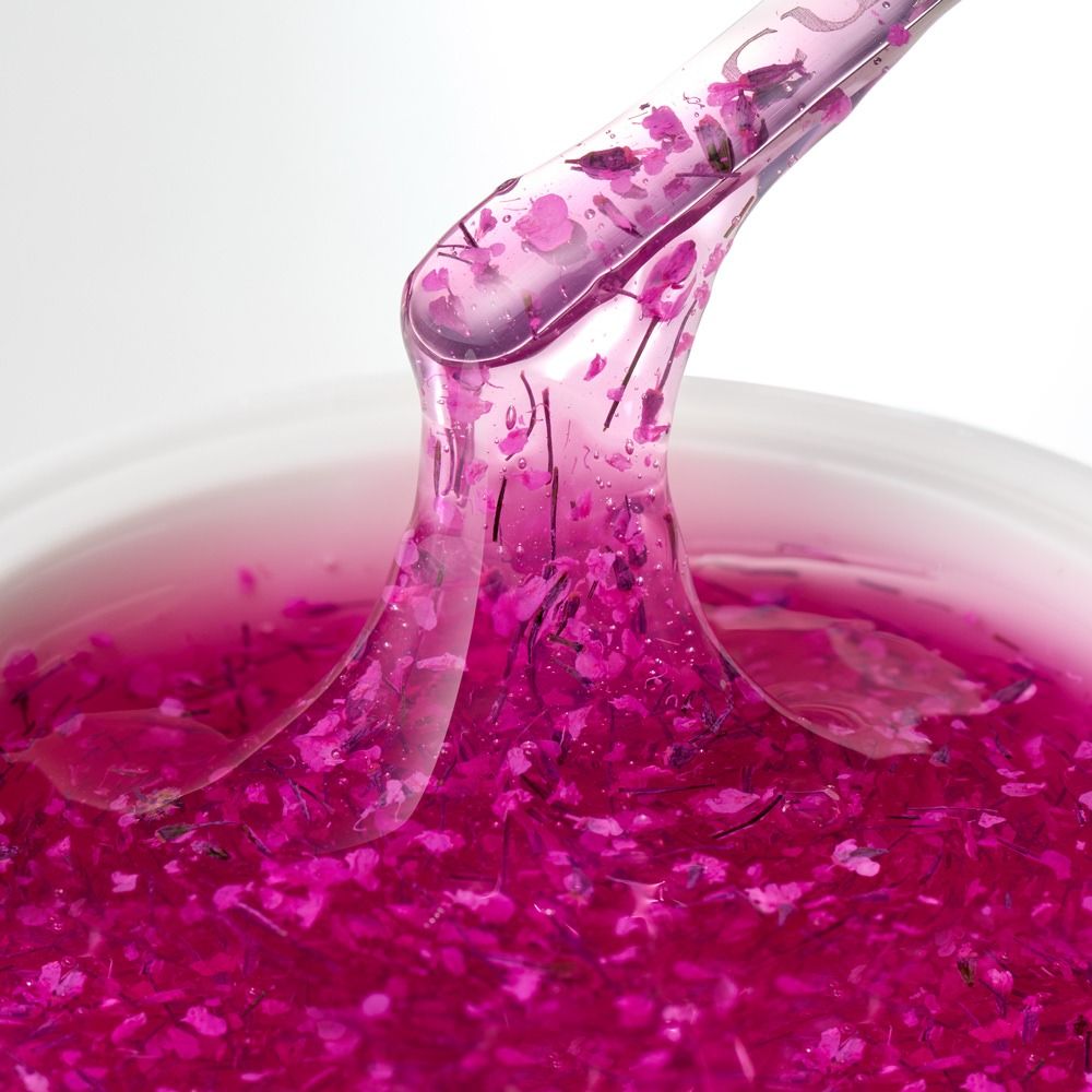 Pinker Gel-Extrakt mit feinen Blütenpartikeln wird mit einem transparenten Spatel aus einem Kosmetiktiegel entnommen