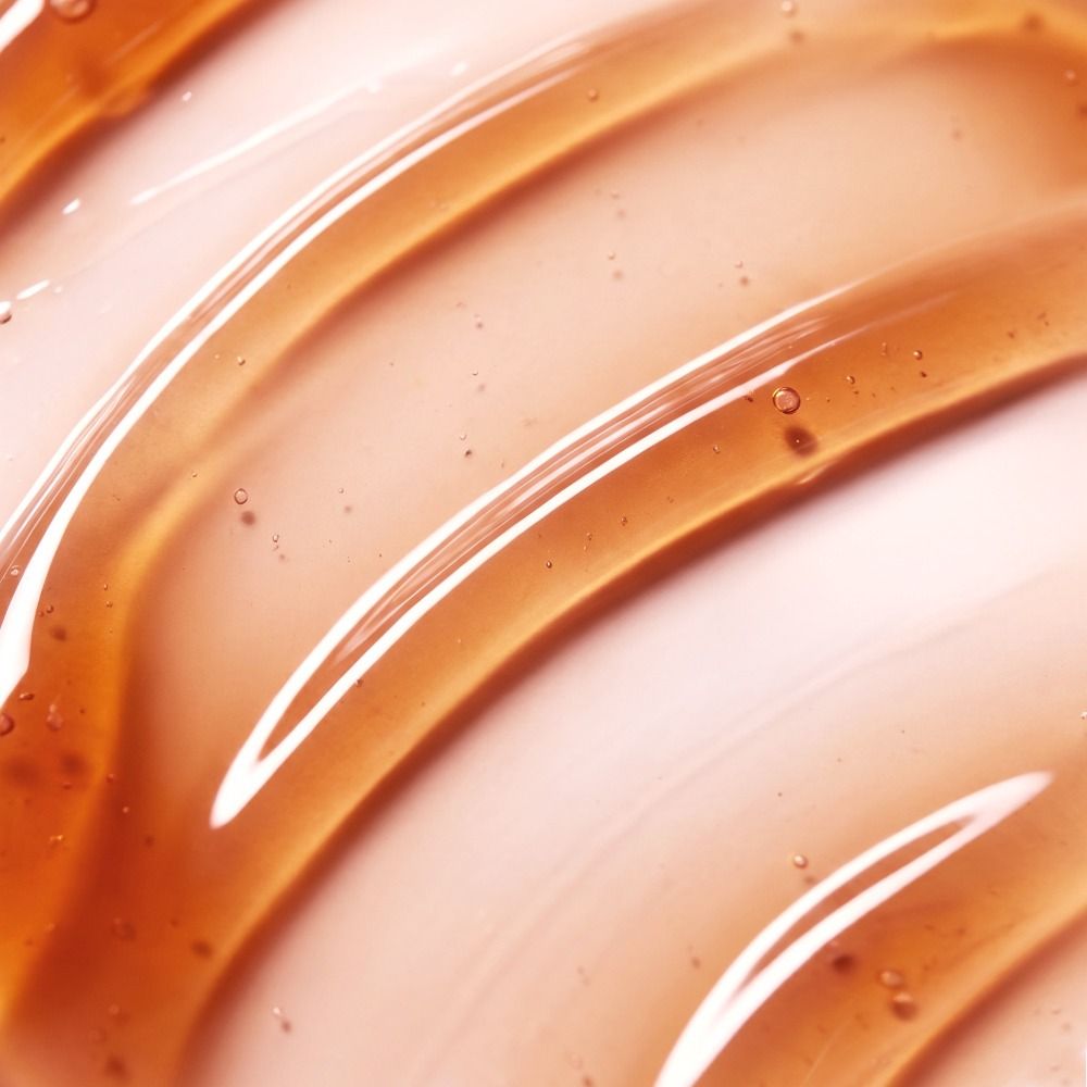 Nahaufnahme einer transparenten, bernsteinfarbenen Kosmetik-Textur als Serum oder Gel mit glänzenden, geschwungenen Linien