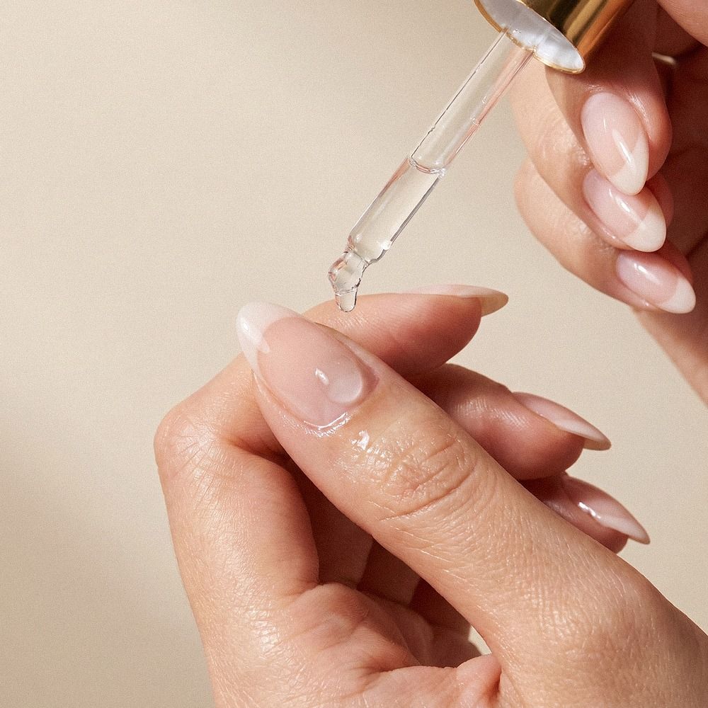 Nahaufnahme einer Pipette mit transparentem Hautpflege-Serum, das auf die Fingerspitze getropft wird – ideal für Gesichtsserum oder Pflegeöl